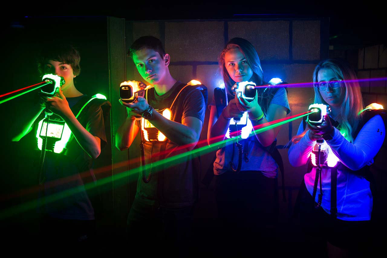 Gruppenbild von zwei Jungen und zwei Mädchen in einer Lasertag Anlage. Sie haben ihre Phaser erhoben und feuern Laserstrahlen ab